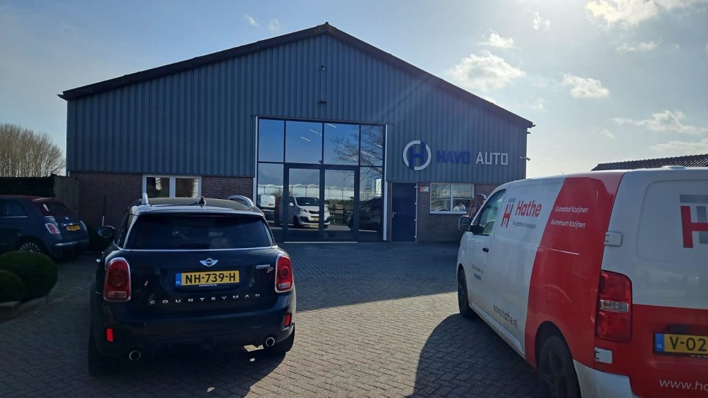 Bedrijfspand van Havo Auto in Poederoijen met een aluminium vliesgevel, met de bus van Hathe ervoor